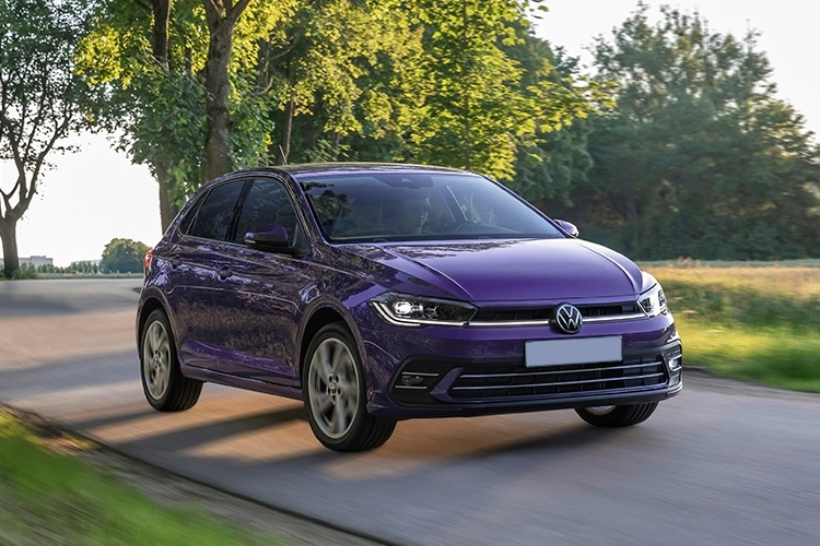 A dark blue Volkswagen Polo driving along a country road.